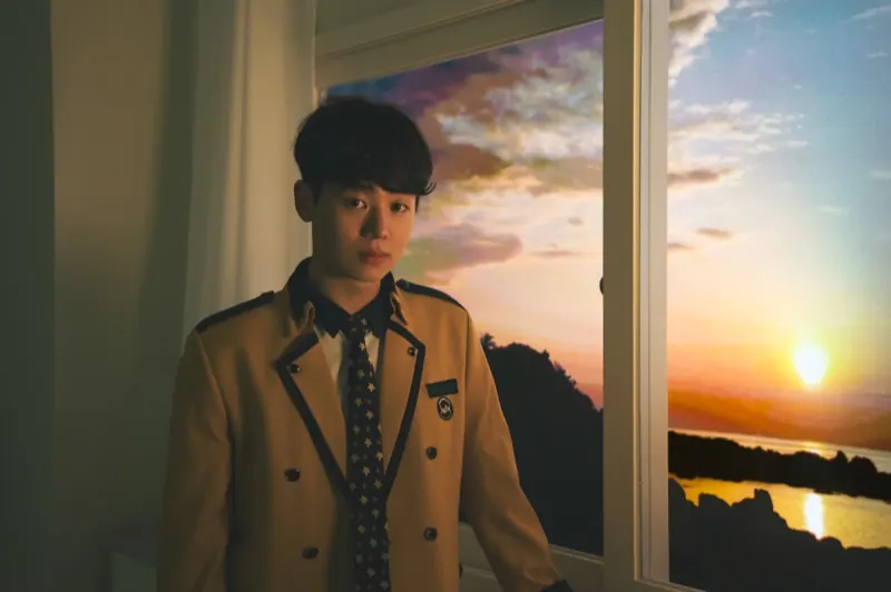 A student in uniform standing by a window with a sunset view